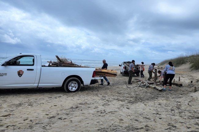 Volunteers and uniformed employees work to pile beach debris into a white pickup truck.