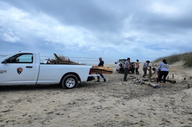 Volunteers with NPS staff at beach cleanup 05-14-2022 Volunteers and uniformed employees work to pile beach debris into a white pickup truck.