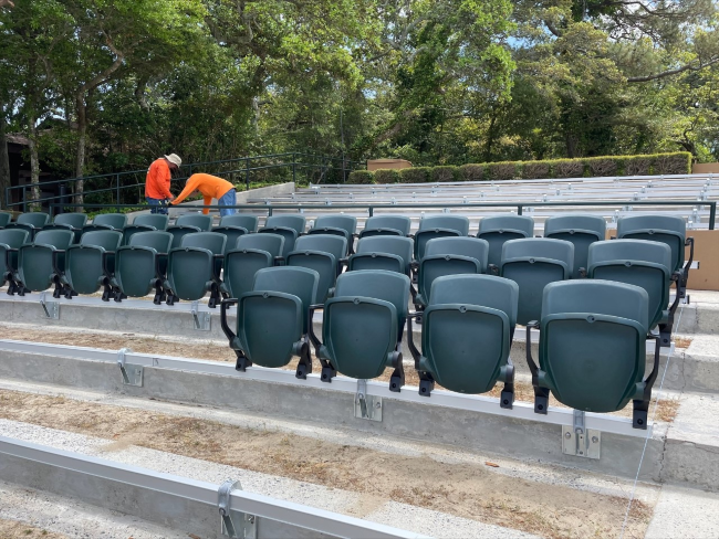 Contractors wearing orange, long-sleeve shirts work to install new seats in an outdoor theater.