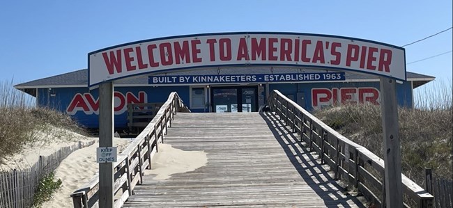 Avon Pier with the name Avon Pier on the building from left to right.  There is also a sign leading up to the boardwalk  "Welcome to America's Pier"