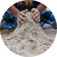 A child sculpts sand with two hands
