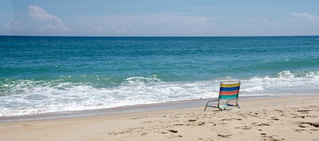 Deep blue waters of the Atlantic Ocean greet the bright tan sands of Cape Hatteras National Seashore where a lone chair waits