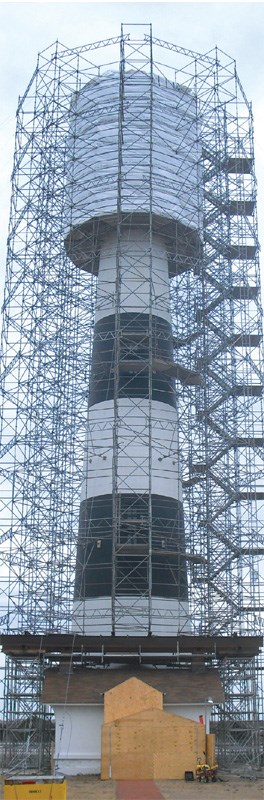 The Bodie Island Lighthouse is surrounded by scafolding, and the lightroom and balcony are enveloped in a wrap to protect them during restoration.