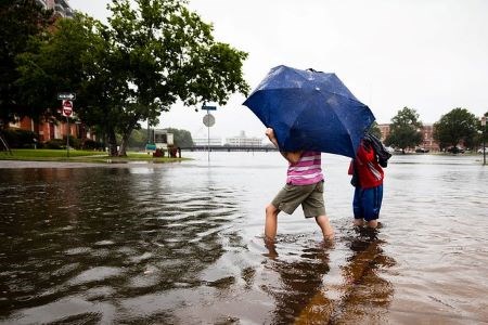 Two people walking in a flood with an umbrella.