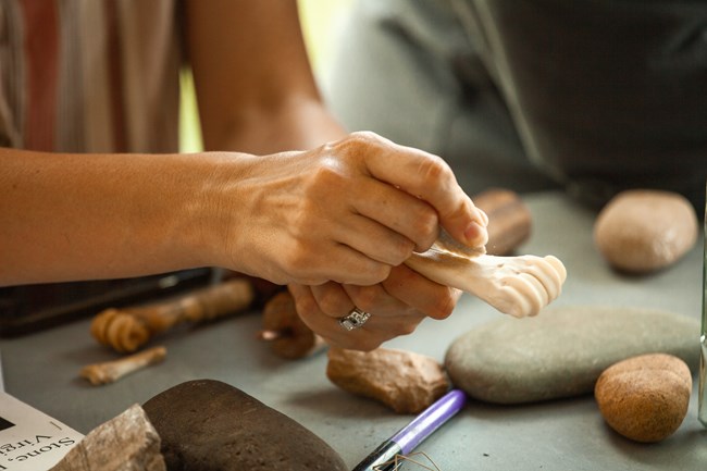 Hands are shown grinding at a skinny animal bone with a piece of rock.