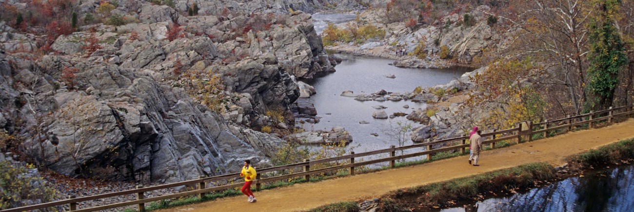 A runner and a couple walking along a trail next to Great Falls on the Potomac River