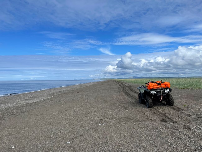 An NPS ATV on the beach of Cape Krusenstern National Monument. Emergency bag is strapped to the ATV with tire tracks in the distance.
