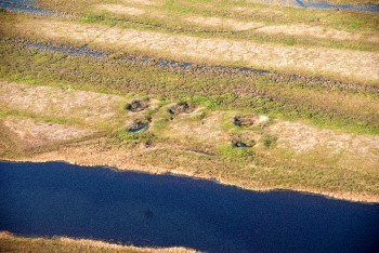 Round holes in the green and tan tundra with water interspersed in the landscape