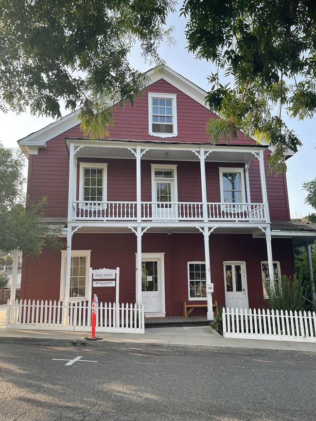Three story house, including attic level. Horizontal plank siding painted dark red. Covered porch and balcony on first two levels