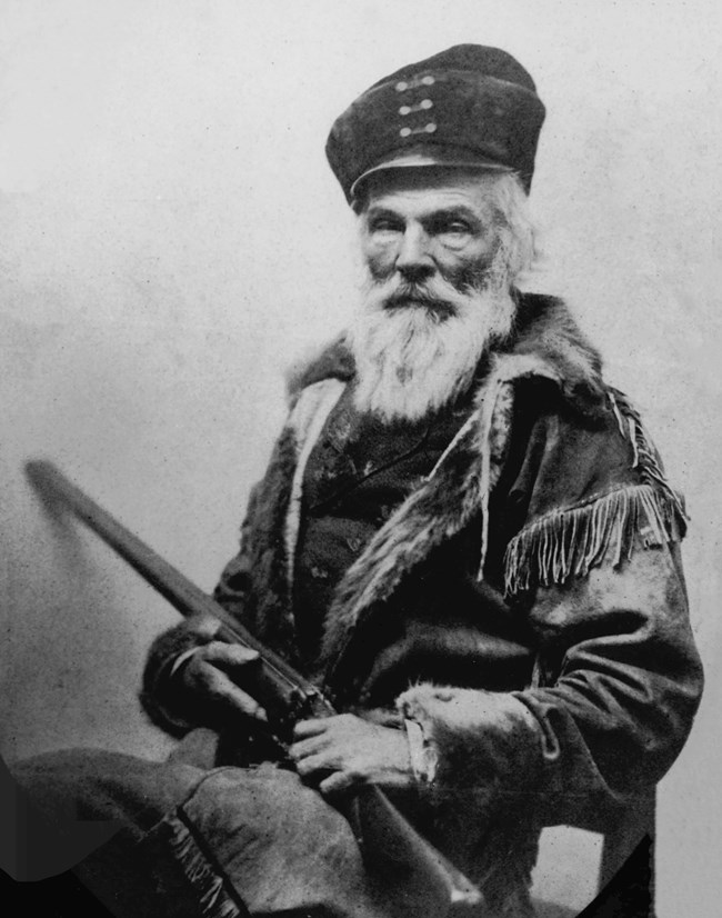 Black and white studio portrait by Matthew Brady. A seated, stern-faced man holds a rifle.
