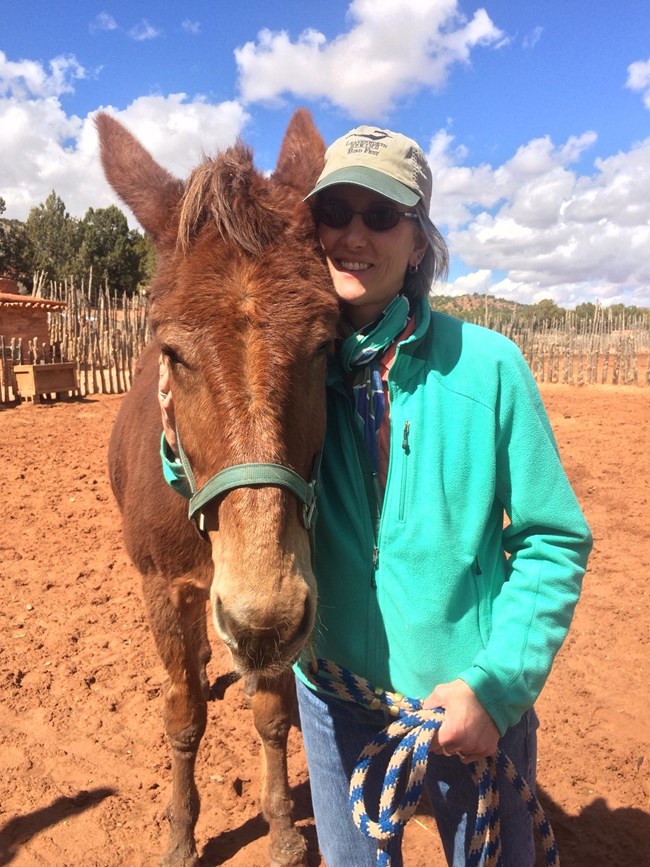 A woman stands next to a mule.