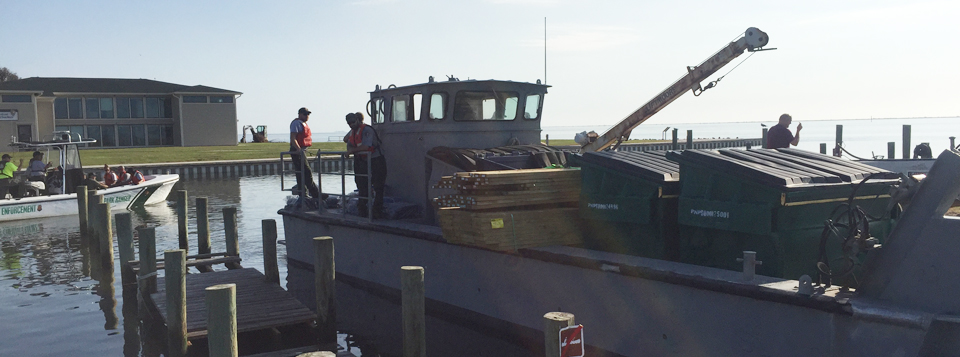 A large crew boat loaded with lumber and other gear prepares to depart as a smaller motor boat departs in the background. A large crew boat loaded with lumber and other gear prepares to depart as a smaller motor boat departs in the background.