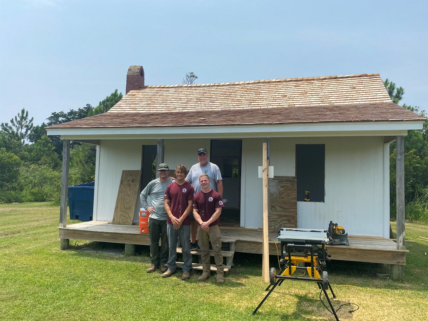 Two NPS Staff and two TTAP interns stand in front of Guthrie-Ogilvie House, with a saw to the right of them.