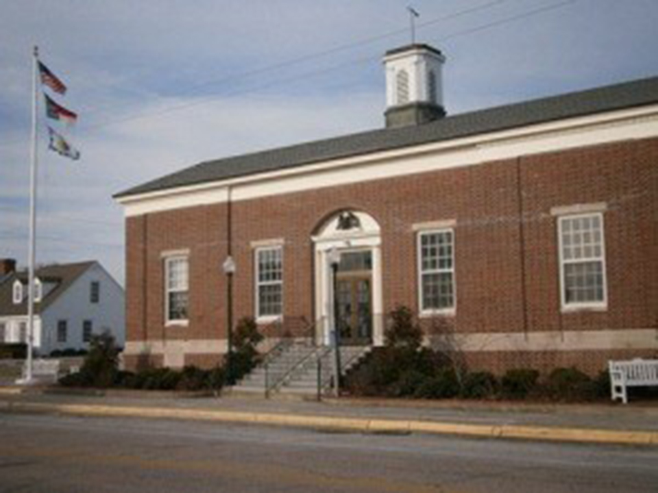 A large brick structure on the edge of a city street with flags flying out front and a cupola on top. A large brick structure on the edge of a city street with flags flying out front and a cupola on top.
