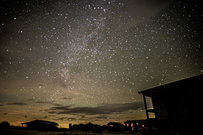 Milky Way above cabins. Sand in foreground.