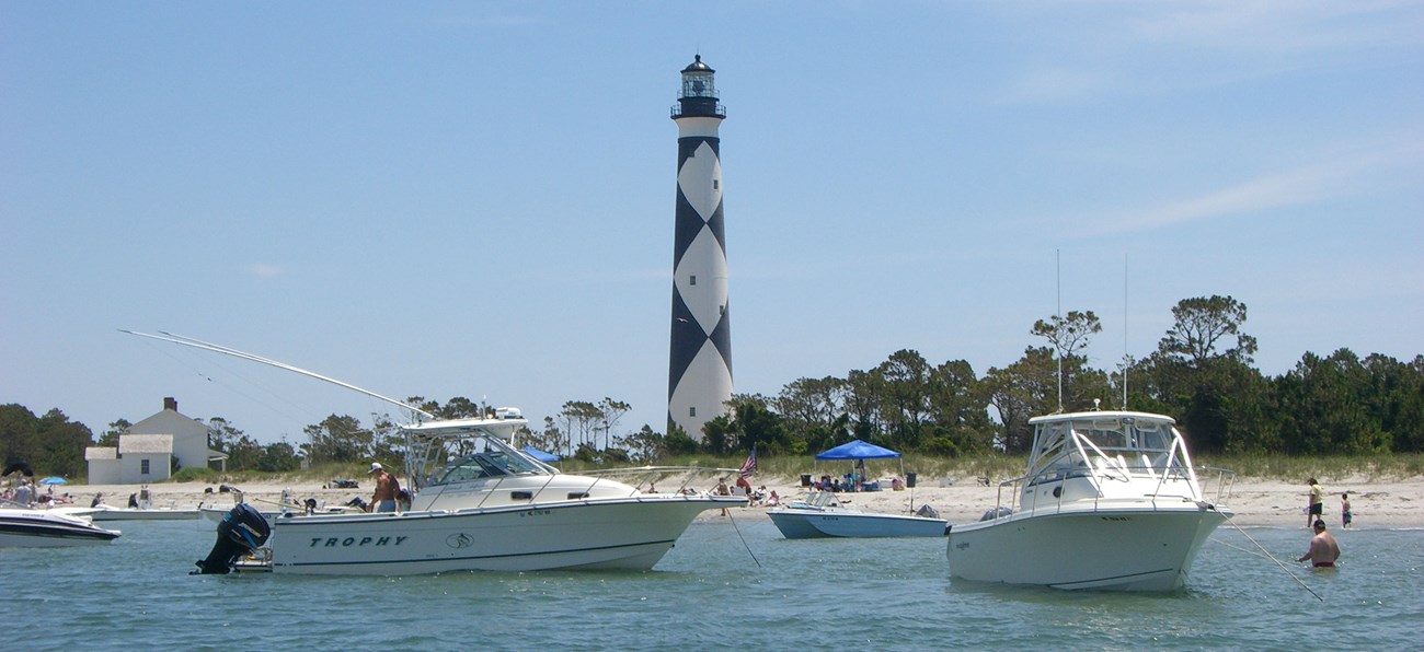 Boats drop anchor in front of the Cape Lookout Lighthouse.
