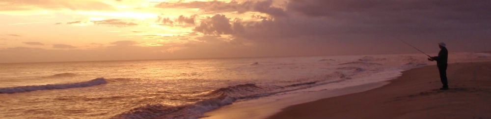 An angler on the beach at sunset.