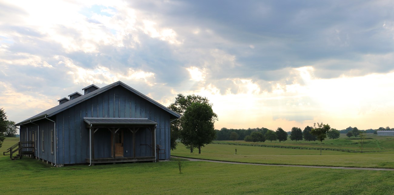 Large wooden reconstructed barracks building amid green fields and trees.
