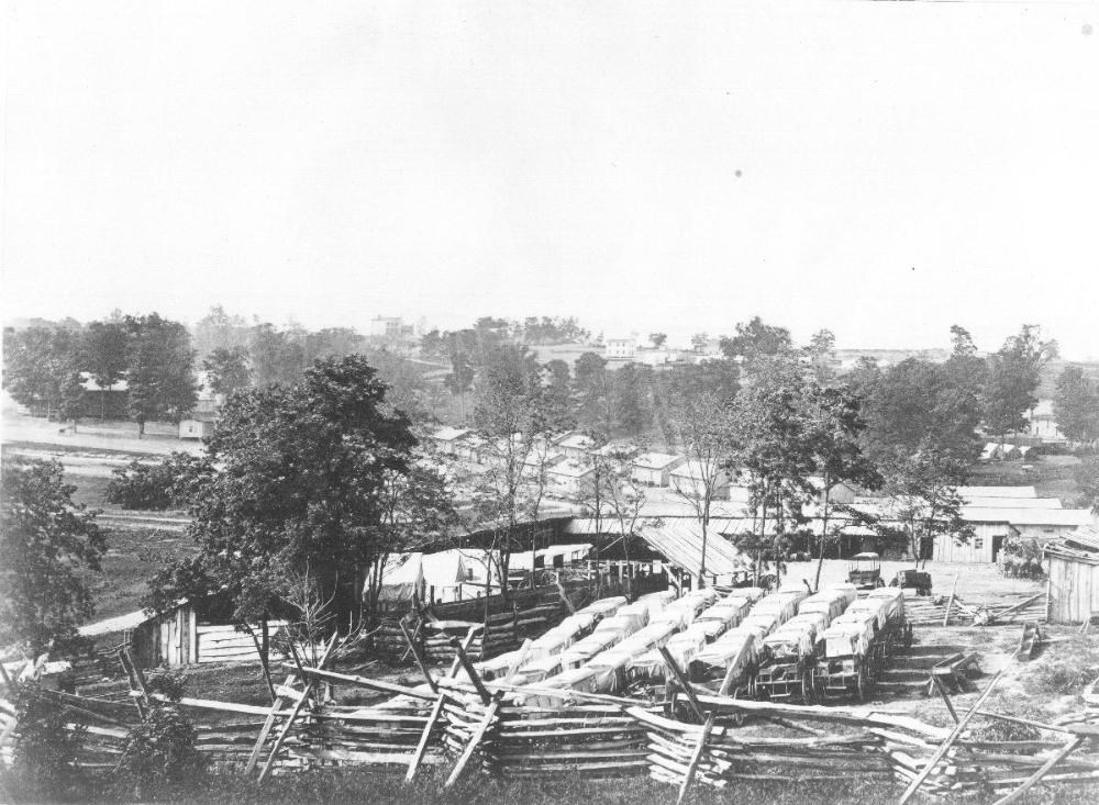 Many wagons and various buildings in the foreground with trees and additional structures in the background during the Civil War.