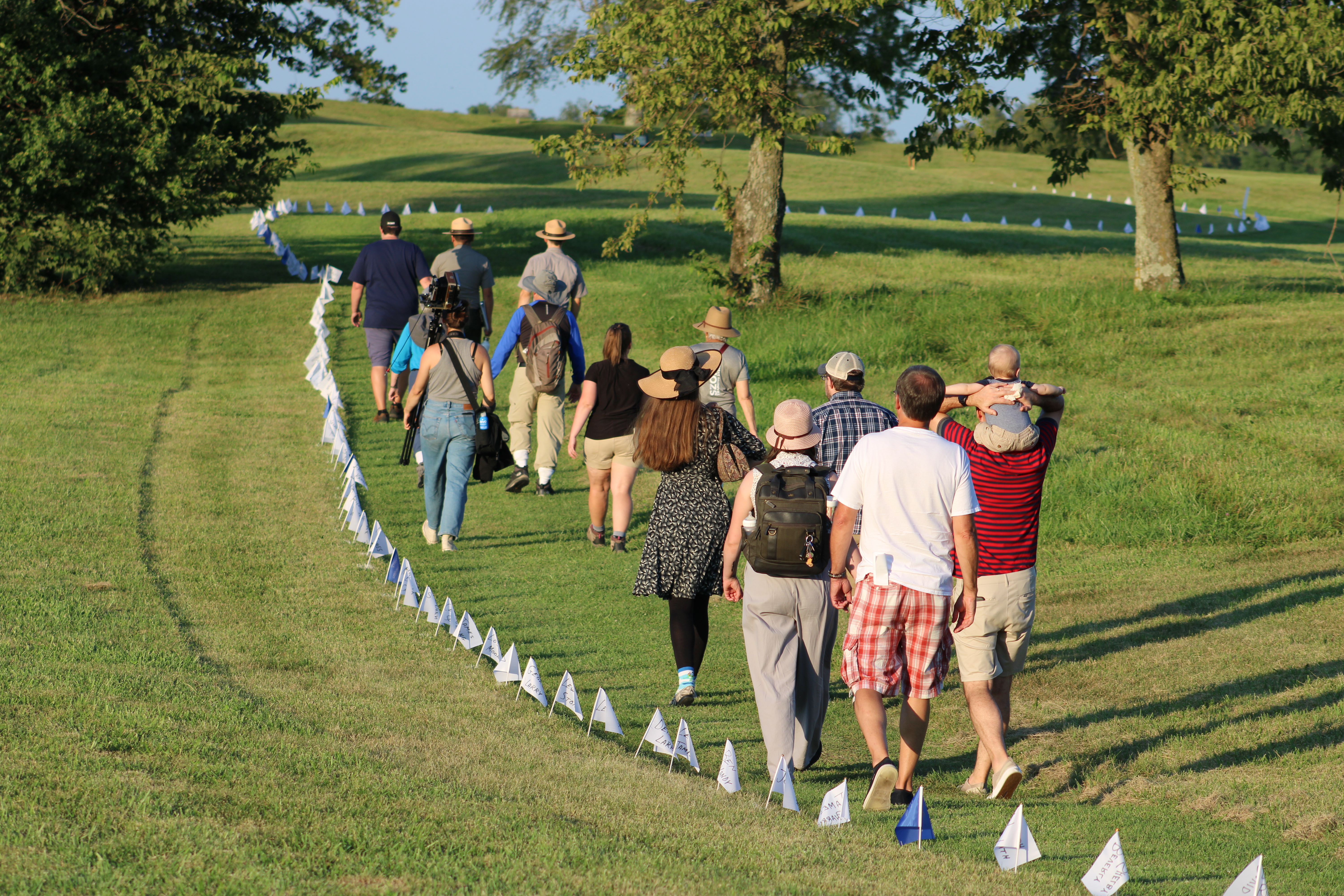Group of people follow two park rangers along a trail lined by small white and blue flags.