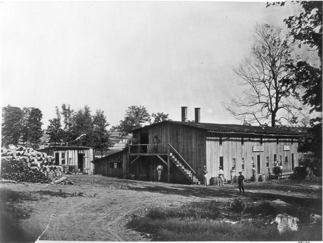 Two-story bakery building with barrels stacked outside and men standing around the structure during the Civil War.