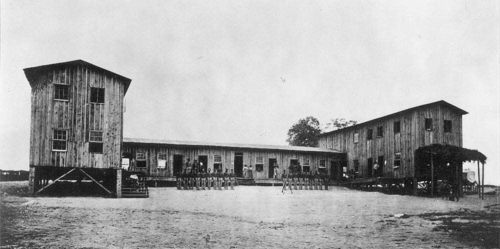 Large wooden barracks building with African American soldiers standing in front of it during the Civil War.