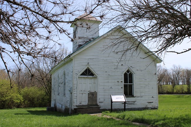 A white wooden church building with a display sign by the front door.