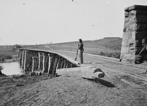 US Soldier nearing a wooden bridge that crosses a water source during the Civil War.