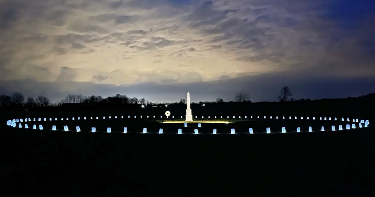 Light bags illuminate a obelisk at night with white clouds.