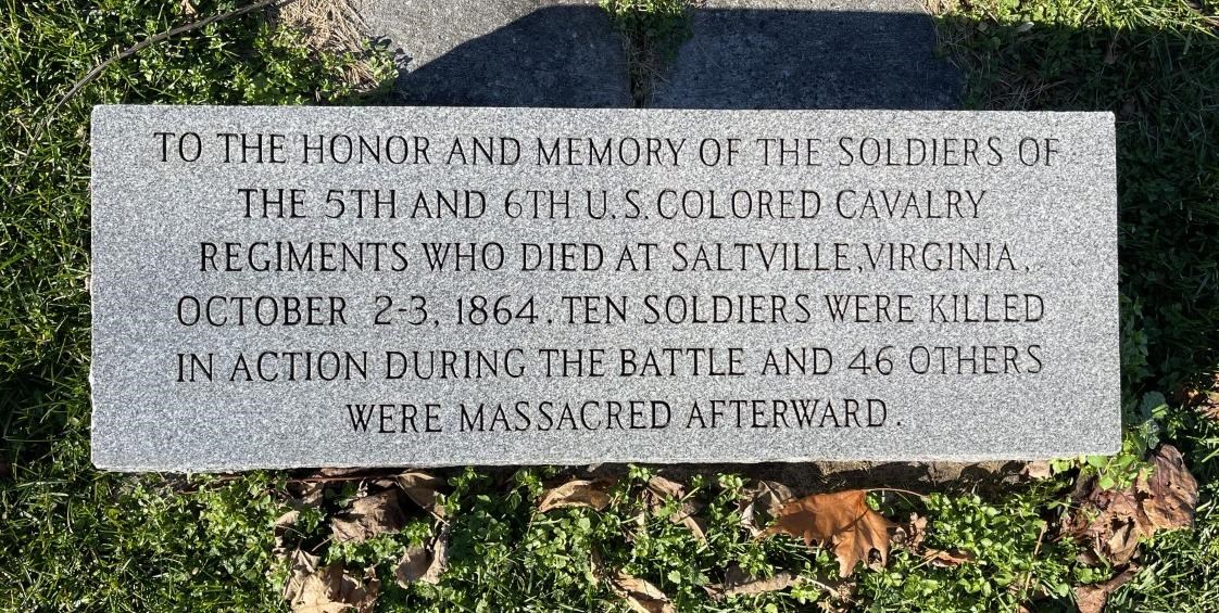 A historic marker that describes the 5th and 6th US Colored Cavalry at the Battle of Saltville, and honoring 46 soldiers who were massacred afterward. The monument sits on green grass with felled leaves around it.
