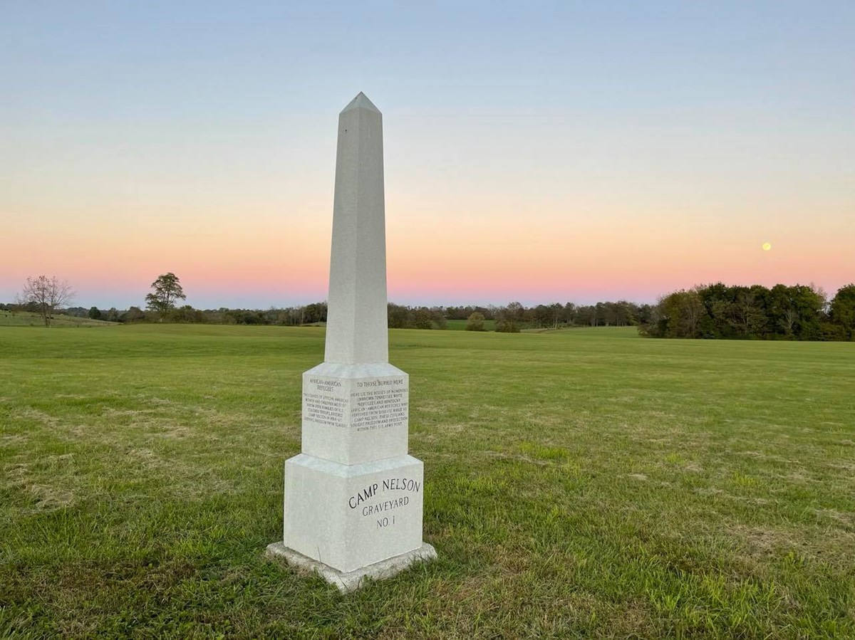 Obelisk surrounded with grass with trees in the background.