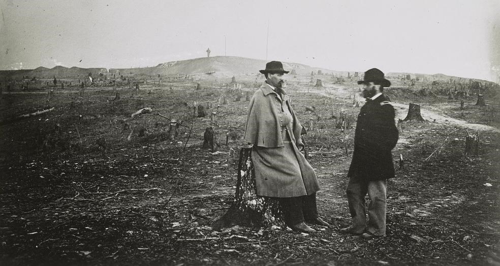 Two US Army officers pose for a photograph at Fort Sanders outside of Knoxville, TN, during the Civil War. Tree stumps and earthworks can be seen in the background.