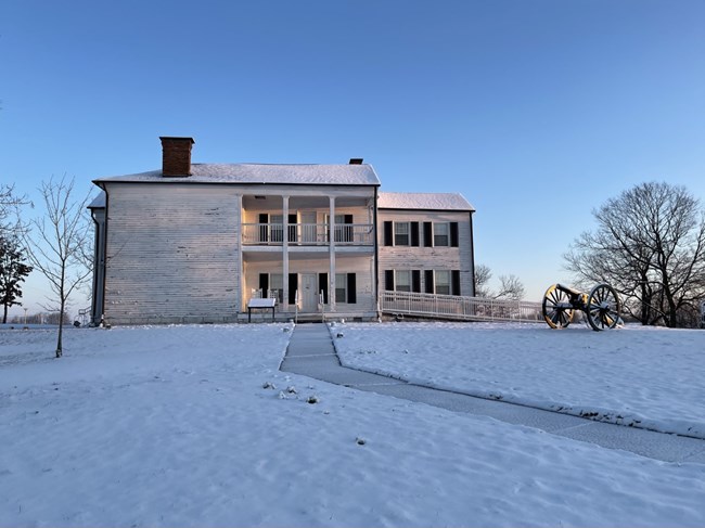 A two-story white building with snow on a ground and leafless trees. A cleared path leads to the front of the structure.
