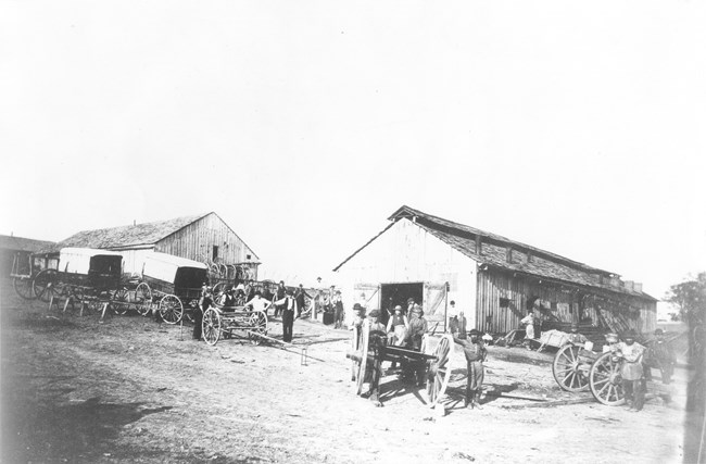 Men standing around wagons with wooden buildings in the background during the Civil War.