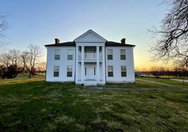 Two-story white building in green field.