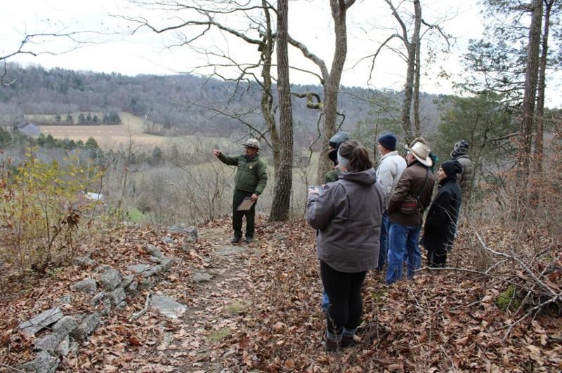 Ranger in woods giving tour to a group of people with broad countryside in background.