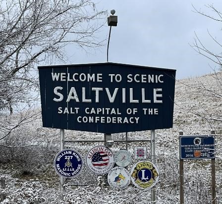 Modern-day welcome sign to Saltville, Virginia, with snowy bushes and trees in the background.