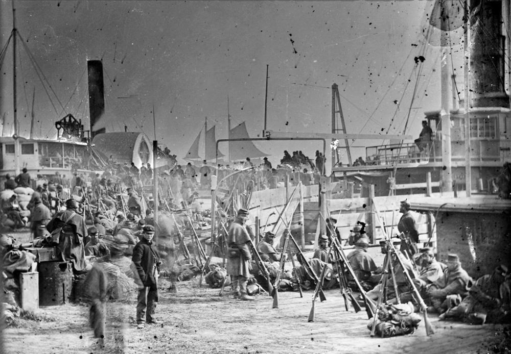 Large crowds of soldiers standing and sitting around while waiting to board steamships during the Civil War.