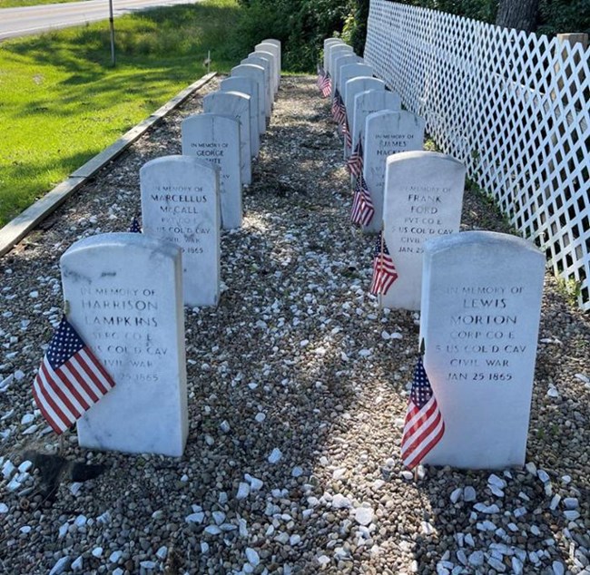 Two rows of white gravestones with woods in background.