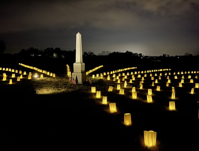 Stone obelisk surrounded by luminaria in dark field.