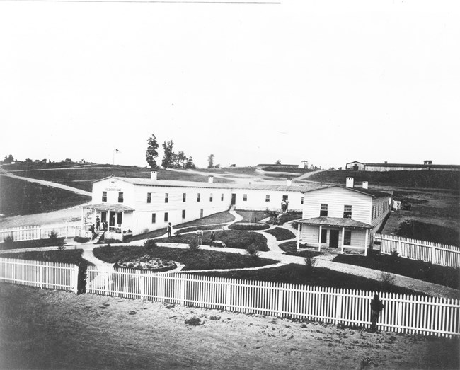 Large U-shaped wooden building with lawns and fences in front.