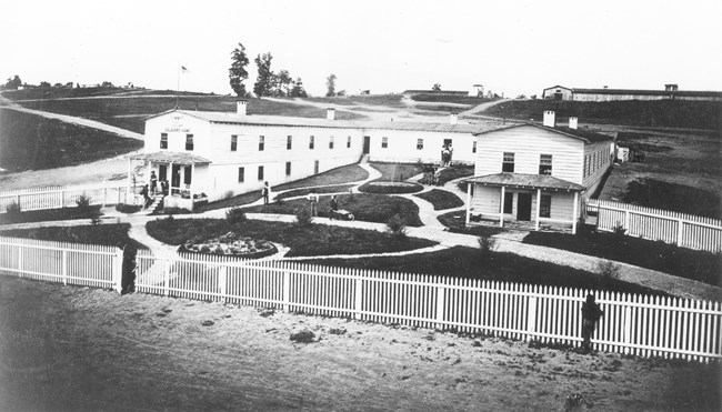 Large U-shaped wooden building with lawns and fences in front.