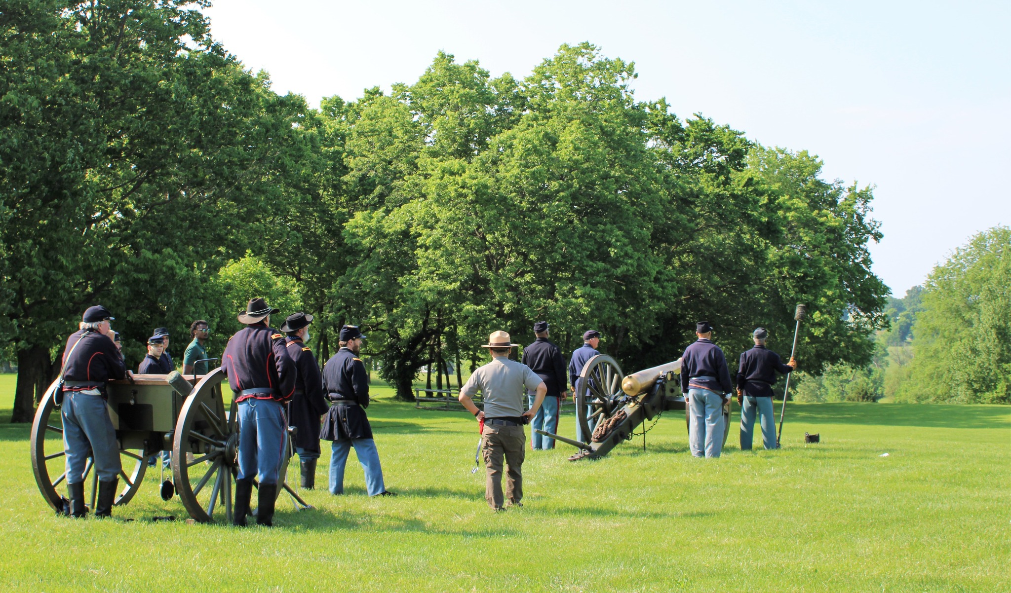 Men in Civil War uniforms and park ranger standing with cannon and limber chest.