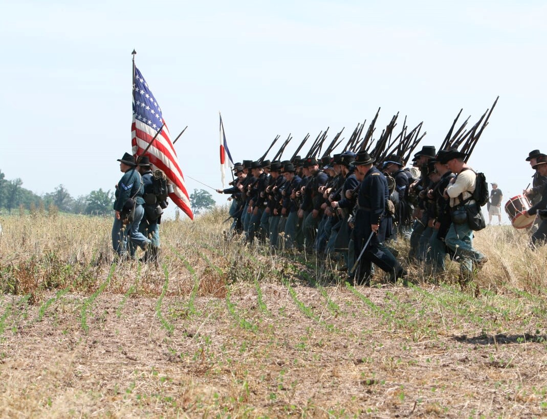 348967499_3246784648801544_6182132691858141585_n Living history interpreters in Civil War military attire march in a line formation.