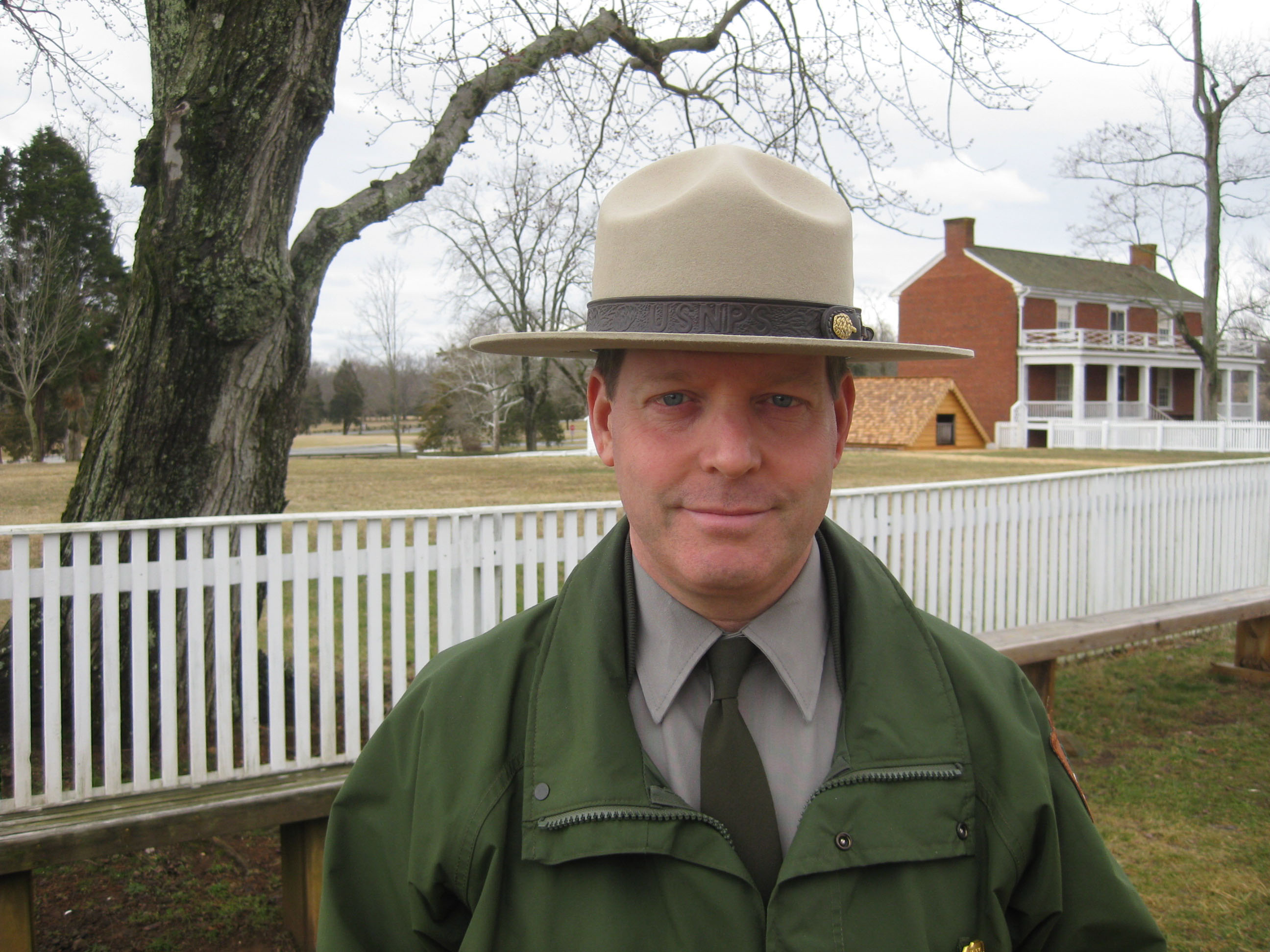 Camp Nelson National Monument Superintendent, Ernie Price A man in a NPS uniform stands in front of a white picket fence and brick home.