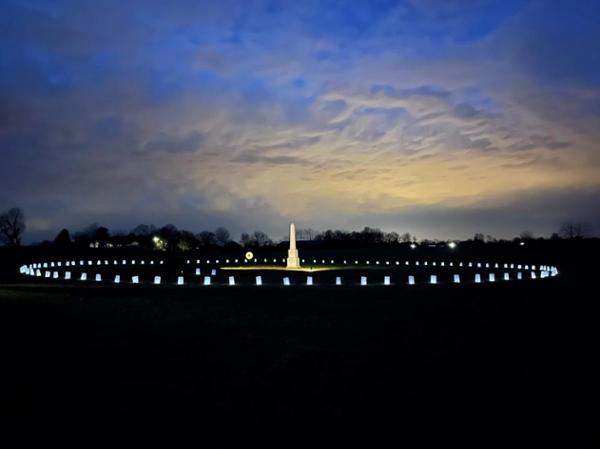 Luminaria White obelisk in an open field surrounded by lit luminaria at night