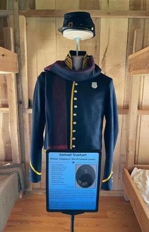 An exhibit featuring a US Army uniform on a mannequin and interpretive text on a panel in a wooden building.