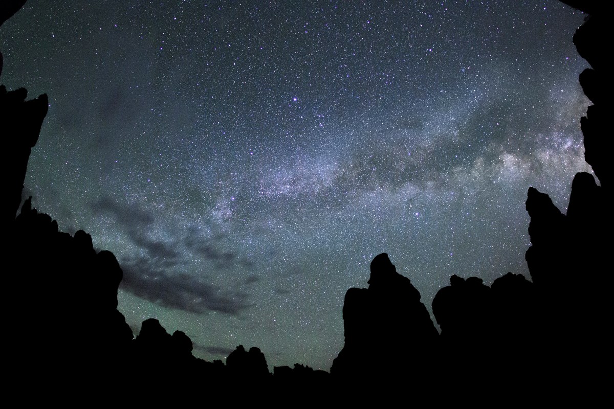 A dense stream of stars arcs across the sky above the silhouettes of rock towers