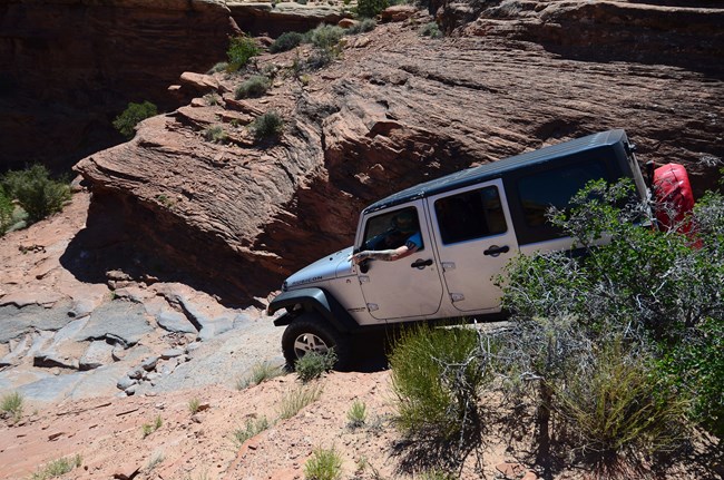 Jeeping in the Needles A white jeep drives down a narrow and steep slickrock road.