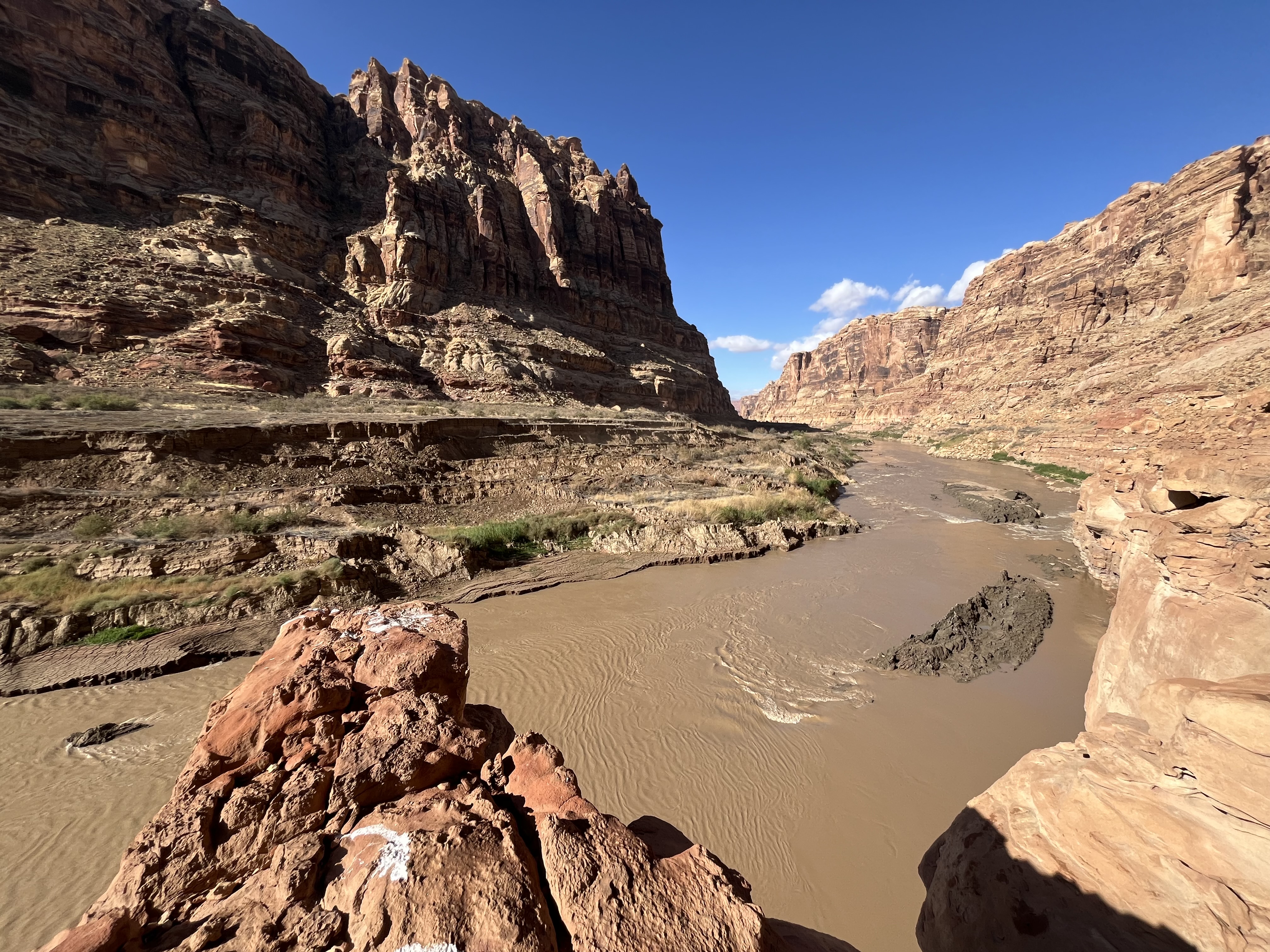 flowing brown water and mud at bottom of rocky river canyon, blue sky above flowing brown water and mud at bottom of rocky river canyon, blue sky above